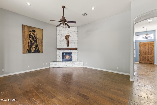 unfurnished living room with a fireplace, dark wood-type flooring, and ceiling fan with notable chandelier