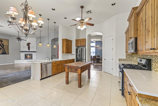 kitchen featuring ceiling fan with notable chandelier, a stone fireplace, light tile patterned floors, and appliances with stainless steel finishes