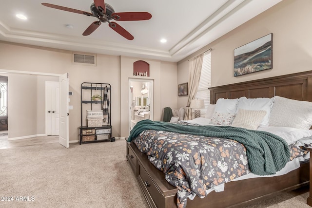 carpeted bedroom with ensuite bathroom, a raised ceiling, and ceiling fan