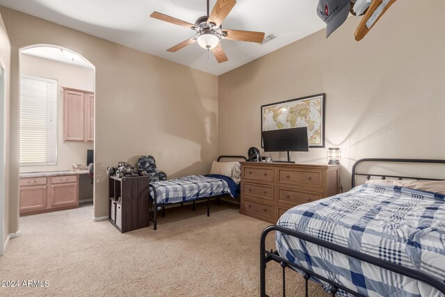 bedroom with ceiling fan, ensuite bathroom, and light carpet