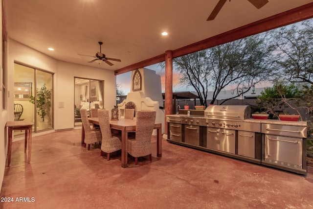 patio terrace at dusk featuring ceiling fan, area for grilling, and an outdoor kitchen