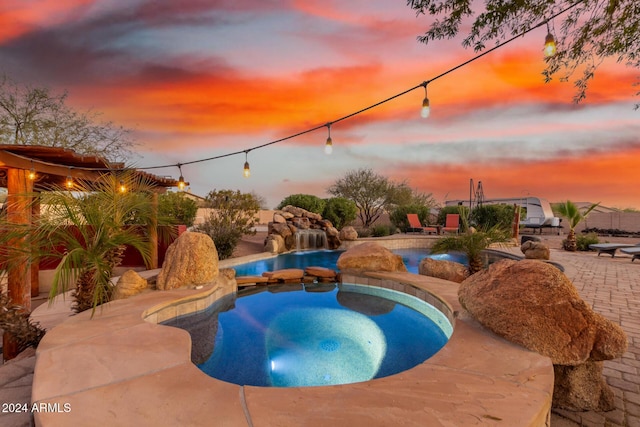 pool at dusk featuring an in ground hot tub and a patio