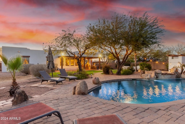 pool at dusk with pool water feature and a patio area