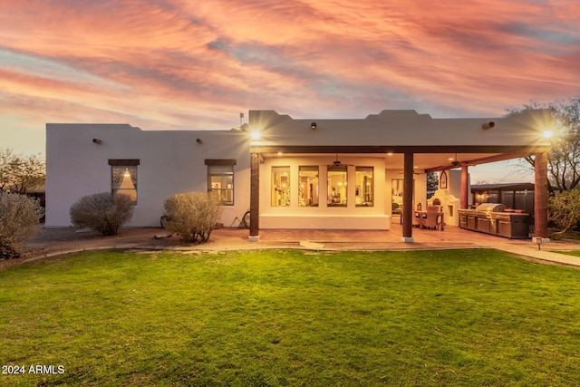 back house at dusk with a yard, a patio area, and exterior kitchen