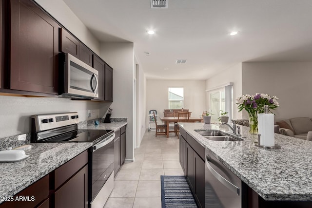 kitchen featuring a center island with sink, visible vents, appliances with stainless steel finishes, light stone counters, and a sink