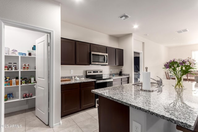 kitchen with light stone counters, dark brown cabinetry, a sink, visible vents, and appliances with stainless steel finishes