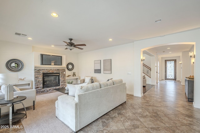 living area featuring stairway, recessed lighting, a fireplace, arched walkways, and a ceiling fan