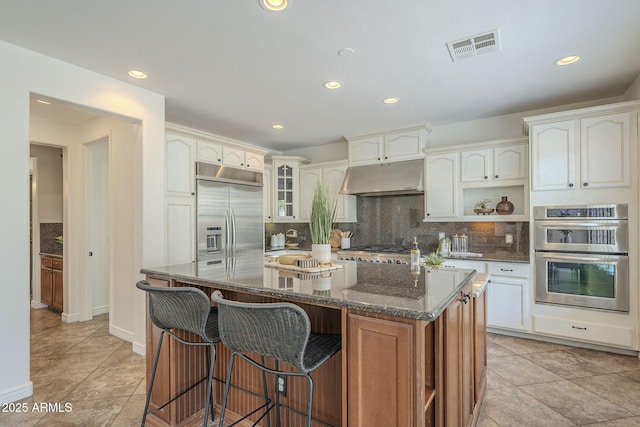 kitchen with visible vents, backsplash, under cabinet range hood, dark stone counters, and appliances with stainless steel finishes