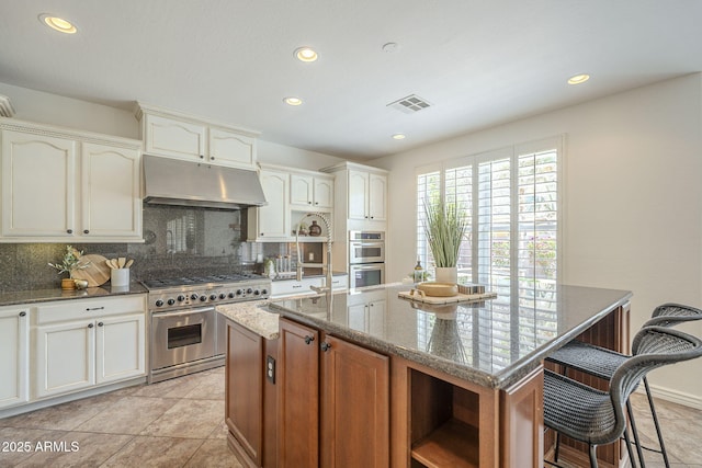 kitchen featuring visible vents, under cabinet range hood, stone countertops, tasteful backsplash, and stainless steel appliances