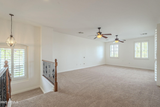 empty room with ceiling fan with notable chandelier, light colored carpet, and visible vents