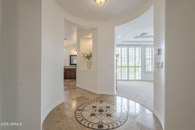 hallway featuring visible vents, baseboards, light colored carpet, and a raised ceiling