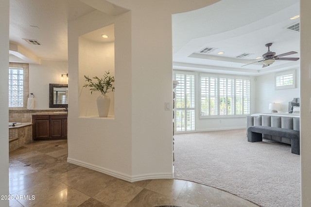 bedroom with a raised ceiling, light colored carpet, visible vents, and baseboards