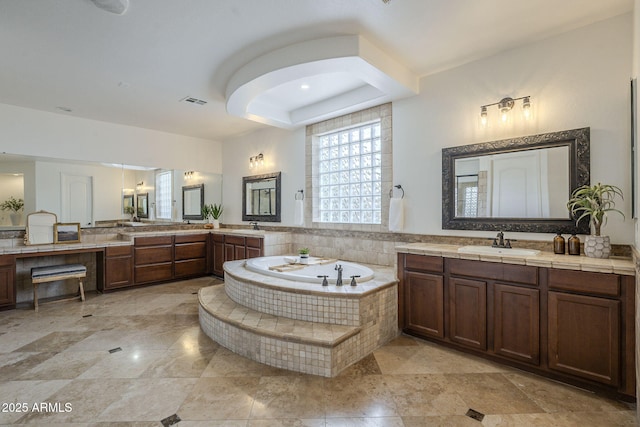 bathroom featuring a sink, a tray ceiling, a garden tub, and two vanities