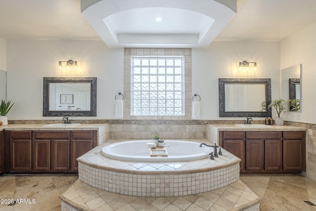 full bathroom featuring two vanities, a garden tub, and a sink