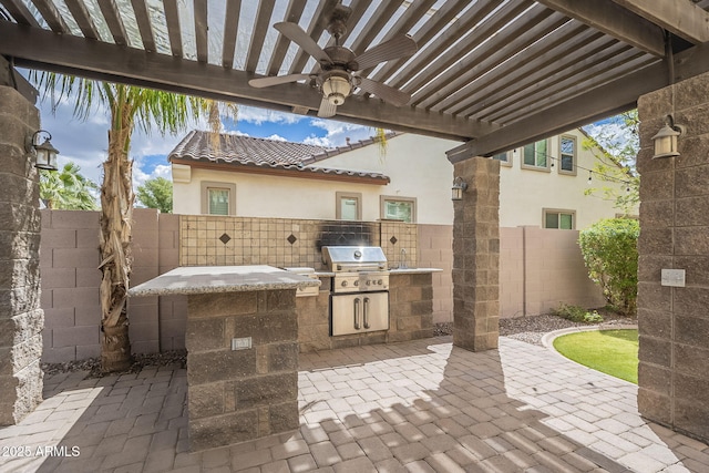 view of patio featuring grilling area, a fenced backyard, an outdoor kitchen, and a ceiling fan