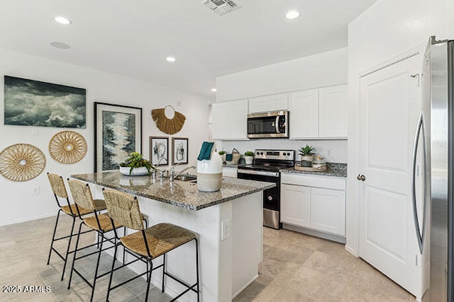 kitchen with a kitchen bar, dark stone counters, an island with sink, stainless steel appliances, and white cabinets