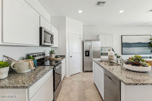 kitchen with sink, appliances with stainless steel finishes, white cabinetry, light stone countertops, and a center island with sink