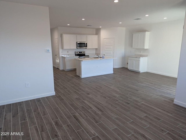 kitchen featuring appliances with stainless steel finishes, white cabinetry, sink, dark wood-type flooring, and a center island with sink