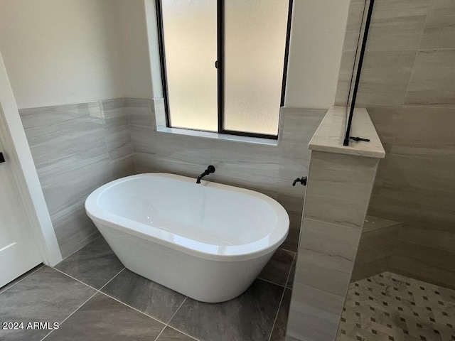 bathroom featuring tile patterned floors, a bath, and tile walls