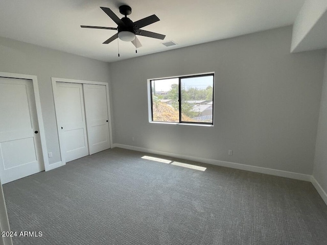 unfurnished bedroom featuring multiple closets, ceiling fan, and dark colored carpet