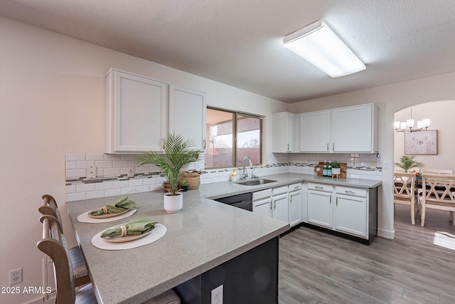 kitchen featuring arched walkways, a peninsula, a sink, white cabinetry, and light wood finished floors