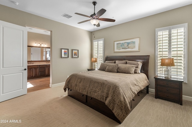 bedroom with ensuite bath, light colored carpet, sink, and ceiling fan