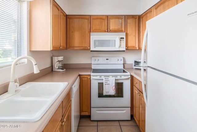 kitchen with brown cabinets, light tile patterned floors, light countertops, a sink, and white appliances