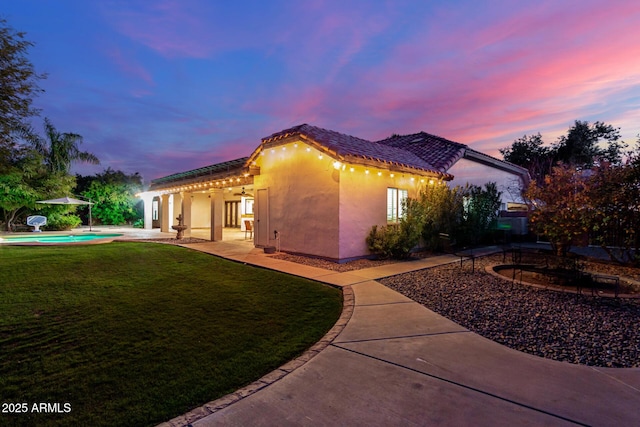 property exterior at dusk with a yard and a patio area