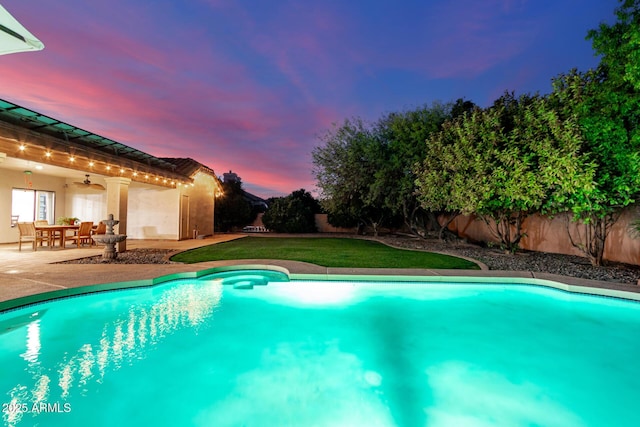 pool at dusk with a patio and ceiling fan