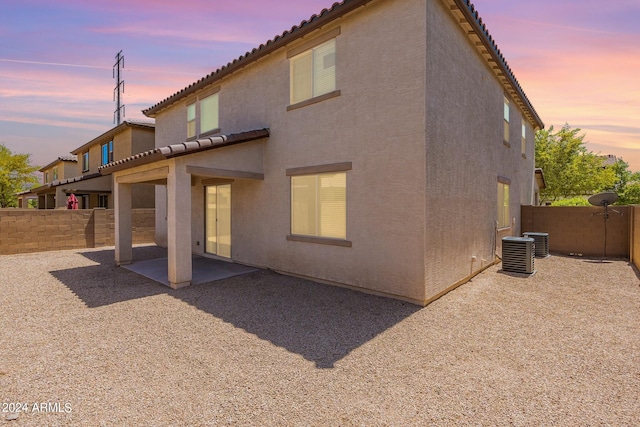 back house at dusk with central AC unit and a patio