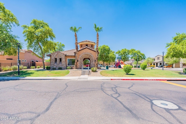 mediterranean / spanish-style home with a front lawn, fence, a tiled roof, stucco siding, and stone siding