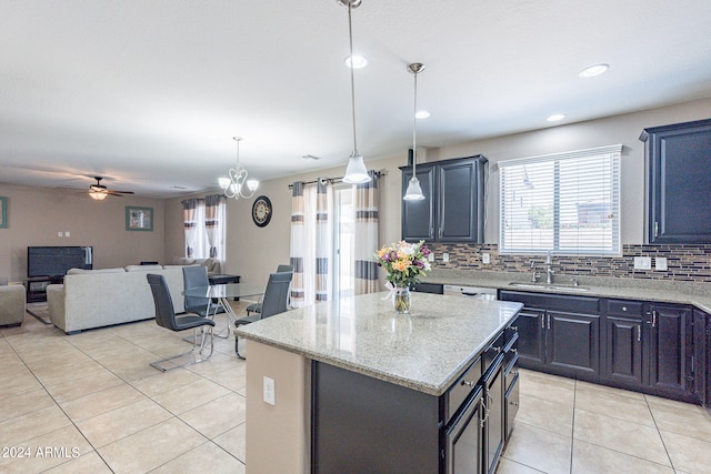 kitchen featuring pendant lighting, ceiling fan with notable chandelier, light stone counters, a center island, and sink