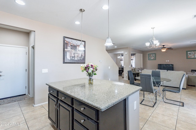 kitchen featuring a center island, light stone counters, ceiling fan with notable chandelier, and decorative light fixtures