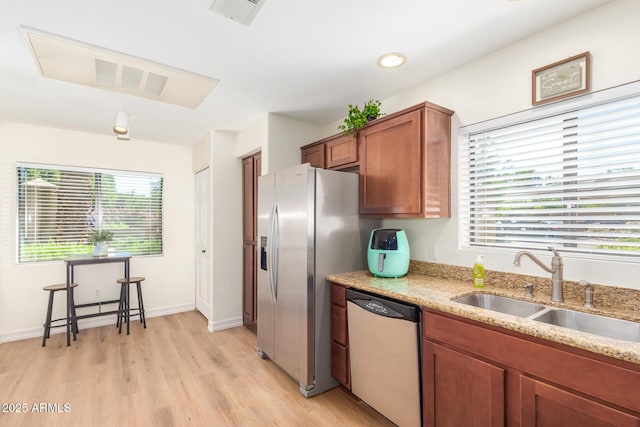 kitchen featuring brown cabinetry, light stone countertops, visible vents, a sink, and stainless steel appliances