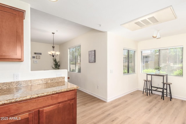 kitchen with light stone countertops, a healthy amount of sunlight, brown cabinetry, and light wood finished floors