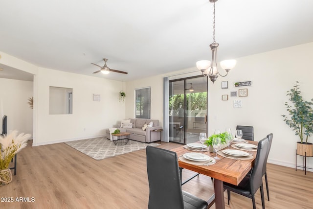 dining space featuring ceiling fan with notable chandelier, baseboards, and light wood-type flooring