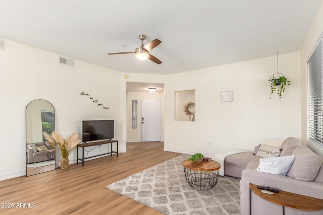 living area with visible vents, baseboards, light wood-style floors, and a ceiling fan