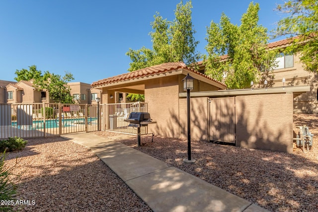 exterior space featuring stucco siding, a patio, fence, a community pool, and a tiled roof