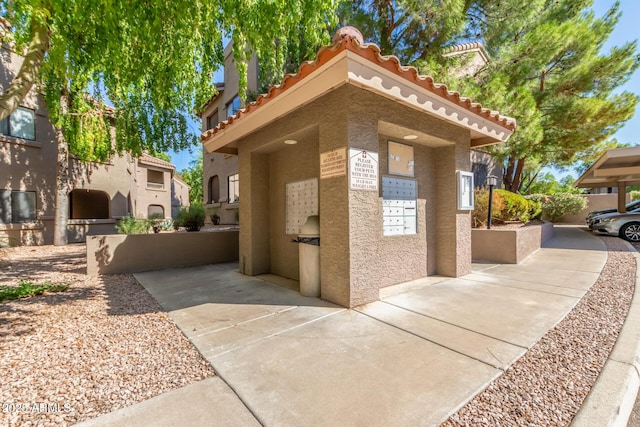 exterior space with a tiled roof, mail area, and stucco siding