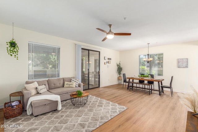 living area featuring ceiling fan with notable chandelier, wood finished floors, and baseboards