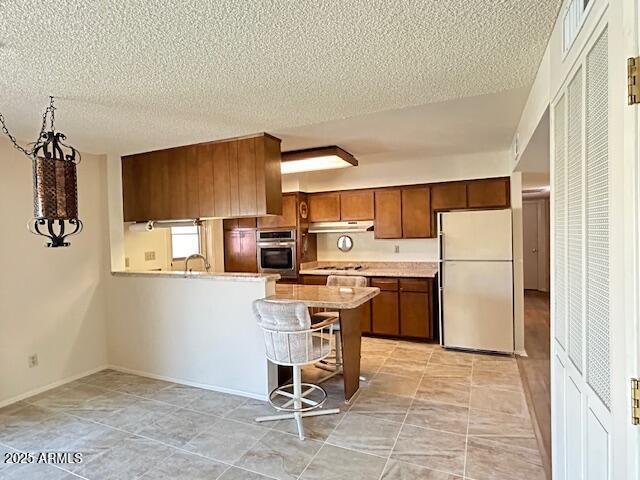 3242 W Christy Dr, Phoenix, AZ 85029 - kitchen with light countertops, freestanding refrigerator, a peninsula, under cabinet range hood, and oven