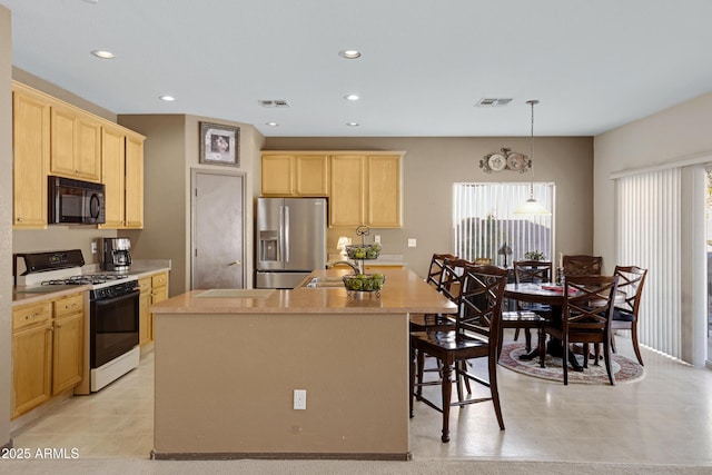 kitchen with a kitchen island, light brown cabinetry, hanging light fixtures, stainless steel fridge, and gas range