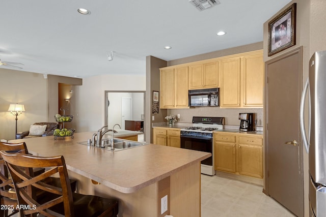 kitchen featuring range with gas cooktop, a kitchen bar, light brown cabinets, sink, and stainless steel fridge