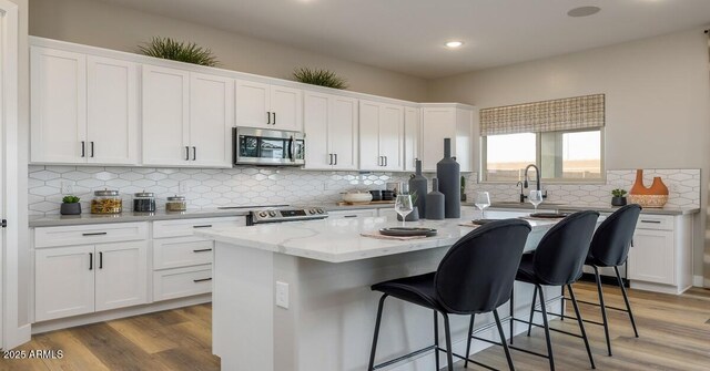 12712 W Corona Ave, Avondale, AZ 85323 - kitchen with stainless steel appliances, a kitchen island, white cabinetry, a kitchen bar, and backsplash