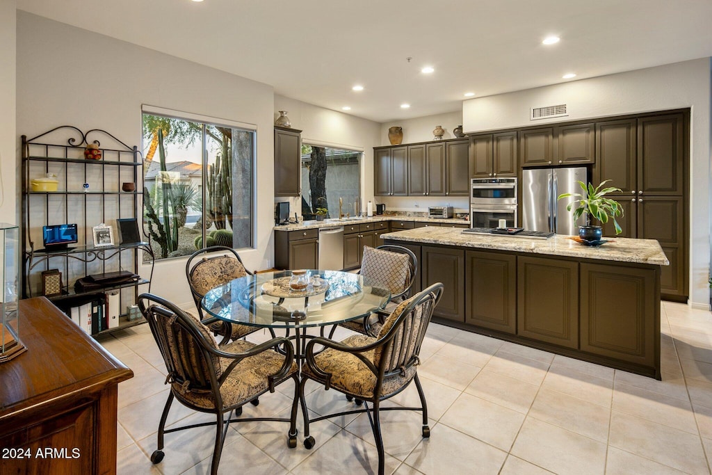 kitchen with light tile patterned floors, sink, a kitchen island, light stone countertops, and appliances with stainless steel finishes