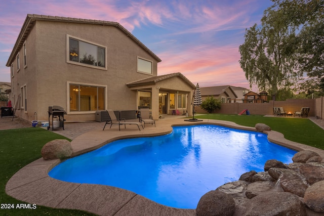 pool at dusk with grilling area, a lawn, and a patio