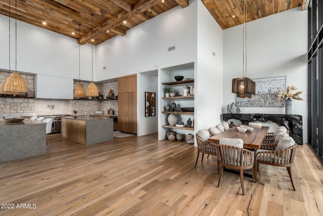 dining area featuring beamed ceiling, a towering ceiling, wooden ceiling, and light hardwood / wood-style floors