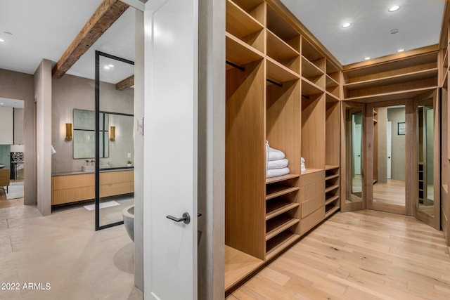 walk in closet featuring beamed ceiling and light hardwood / wood-style flooring