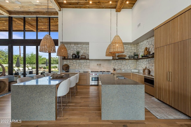 kitchen featuring decorative backsplash, a kitchen island with sink, wood-type flooring, beamed ceiling, and stainless steel stove