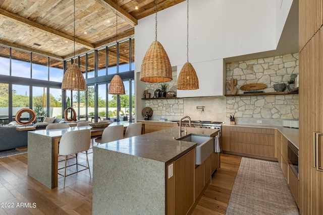 kitchen featuring a towering ceiling, a kitchen island with sink, sink, wood-type flooring, and beamed ceiling